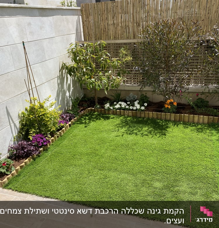 גינה עם דשא, פרחים ועצים קטנים לאורך הגדר